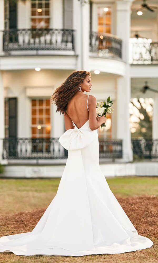 Martina Liana Design: Rückenansicht einer Braut im schlichten Kleid mit großer Schleife, vor einem eleganten, historischen Gebäude.