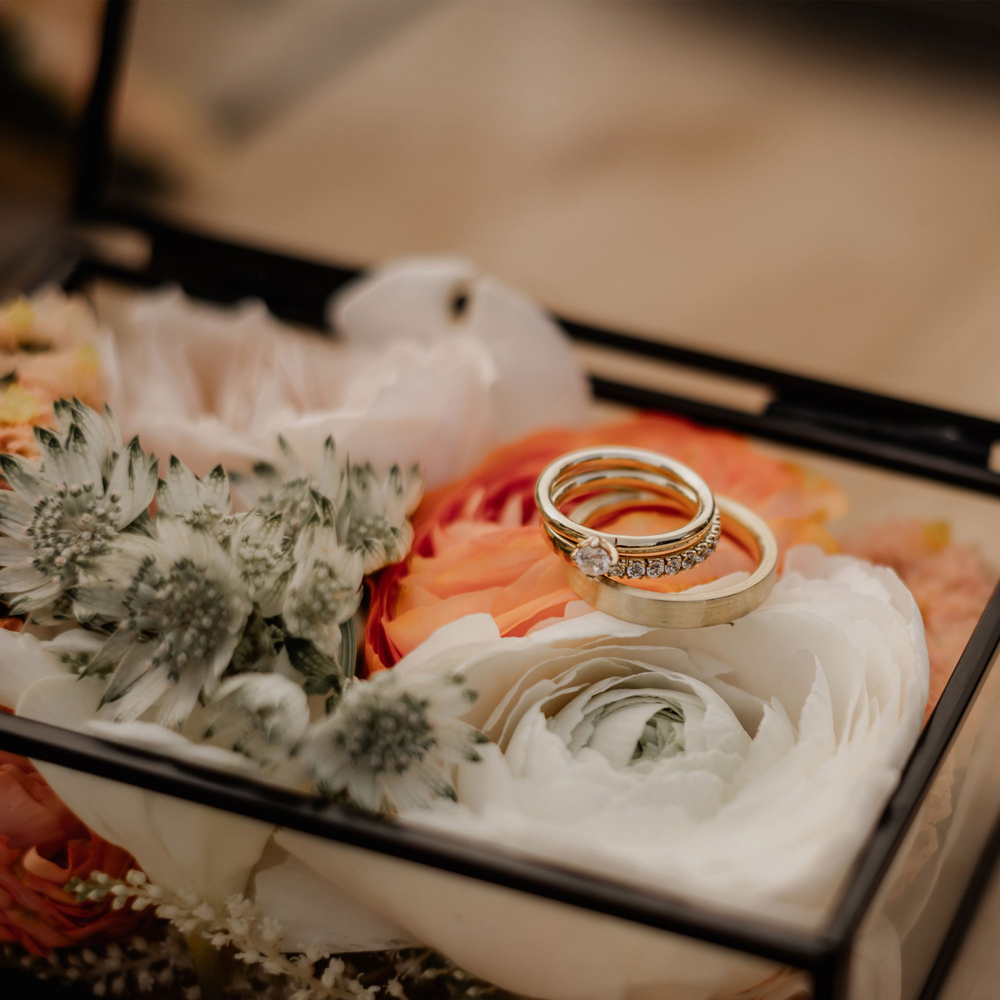 Gläserne Box mit Blumendekoration in Pastelltönen, in der zwei Eheringe stilvoll präsentiert werden.