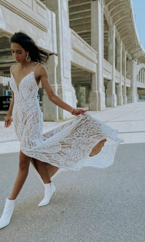 Braut in einem lässigen, boho-spitzenbesetzten Kleid mit weißen Stiefeletten, fotografiert unter einer modernen, städtischen Brücke.
