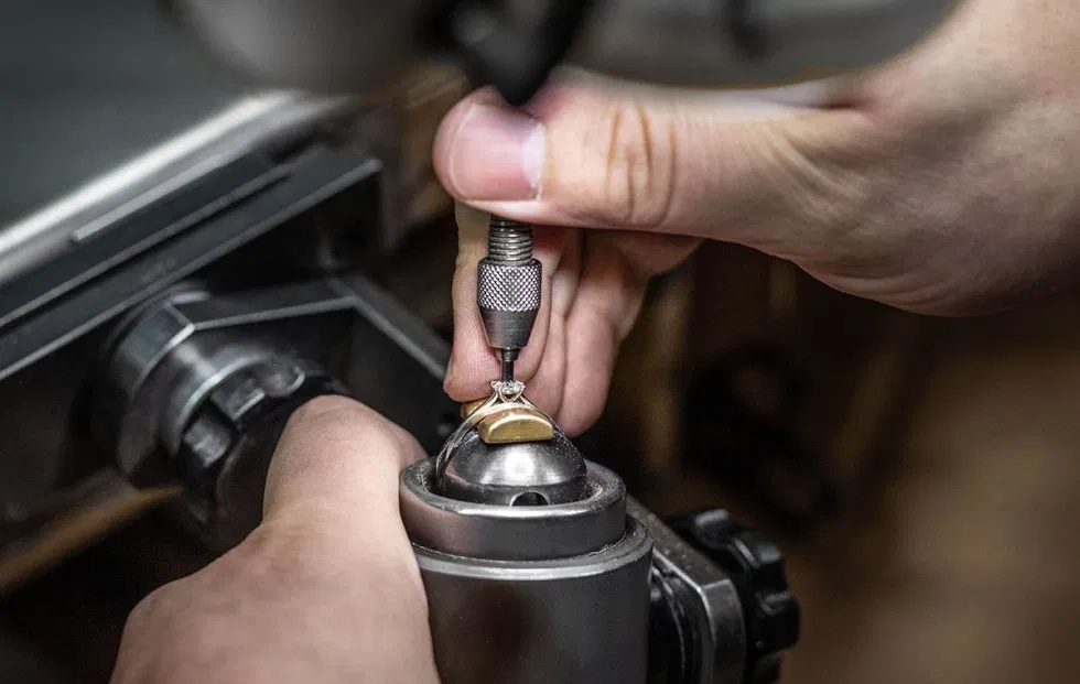 Arbeitsschritt in der Schmuckmanufaktur: Ein Ring wird maschinell bearbeitet, Hände des Goldschmieds bei der präzisen Verarbeitung.