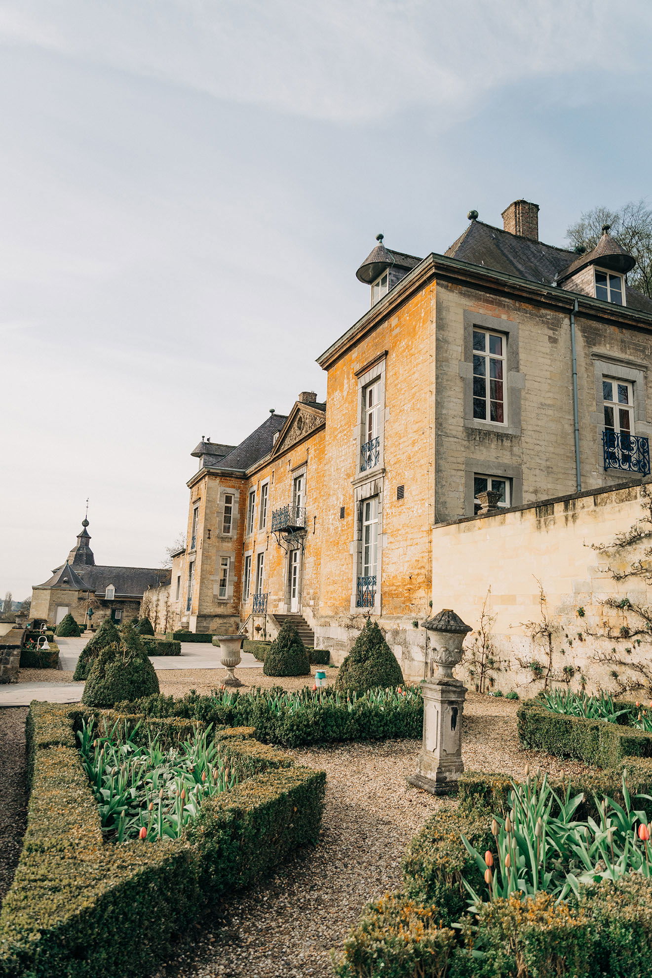 Elegantes Landhaus aus Stein mit symmetrischen Hecken und Tulpenbeeten im Garten, eine malerische Kulisse für Hochzeitsfeiern.