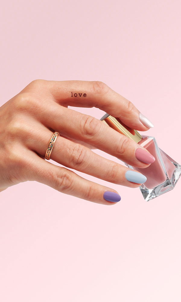 Farblich abgestimmte Nägel in Rosa, Blau und Lila, dazu ein goldener Ring und das Wort "love".