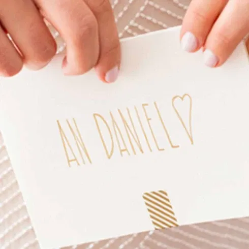 Nahaufnahme einer Braut, die einen Liebesbrief mit der Aufschrift „An Daniel“ hält. Der Brief ist in goldener Schrift verziert und wirkt besonders liebevoll.