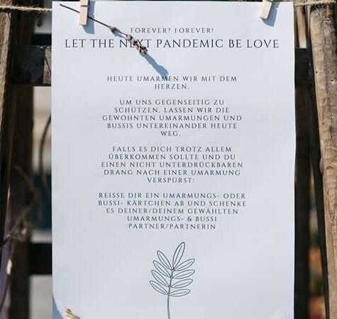 Ein Schild mit der Aufschrift 'Let the next pandemic be love', das humorvoll zum Verzicht auf Umarmungen und stattdessen auf symbolische Gesten hinweist.