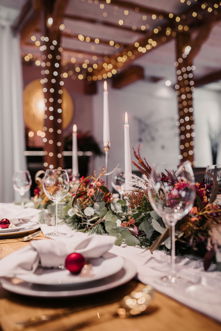 Weihnachtlich dekorierter Hochzeitstisch mit hohen weißen Kerzen und Blumenarrangements, die in warmem Kerzenschein erstrahlen.