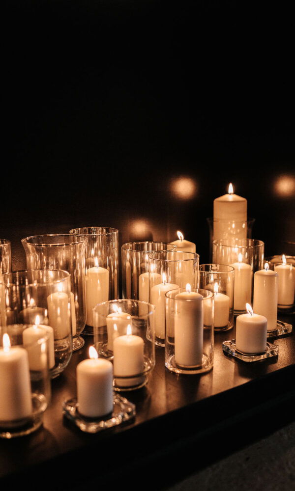 Ein Arrangement aus verschiedenen weißen Kerzen in Gläsern, die in einem dunklen Raum für eine romantische und festliche Stimmung sorgen.