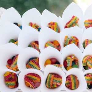 Ein Tablett voller kegelförmiger Verpackungen mit bunten Gummibändern und Süßigkeiten, arrangiert auf einem Festtisch mit anderen Süßigkeiten und einer Tiara im Hintergrund.
