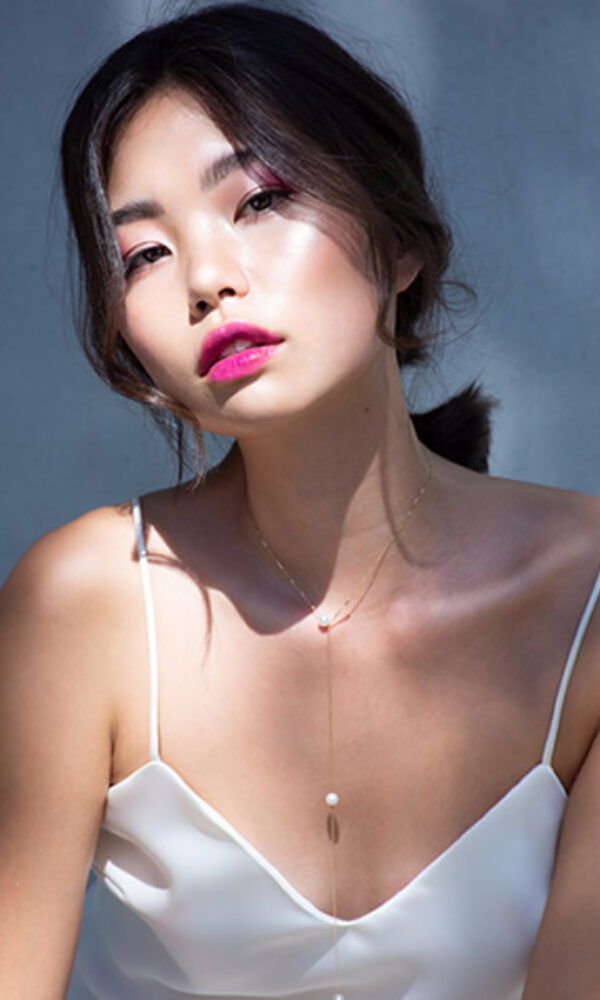 Junge Frau mit zurückgestecktem Haar und auffälligem Make-up, inklusive einem kräftigen, pinken Lippenstift. Ihr schlichtes, elegantes Top hebt die Raffinesse ihres Looks hervor.
