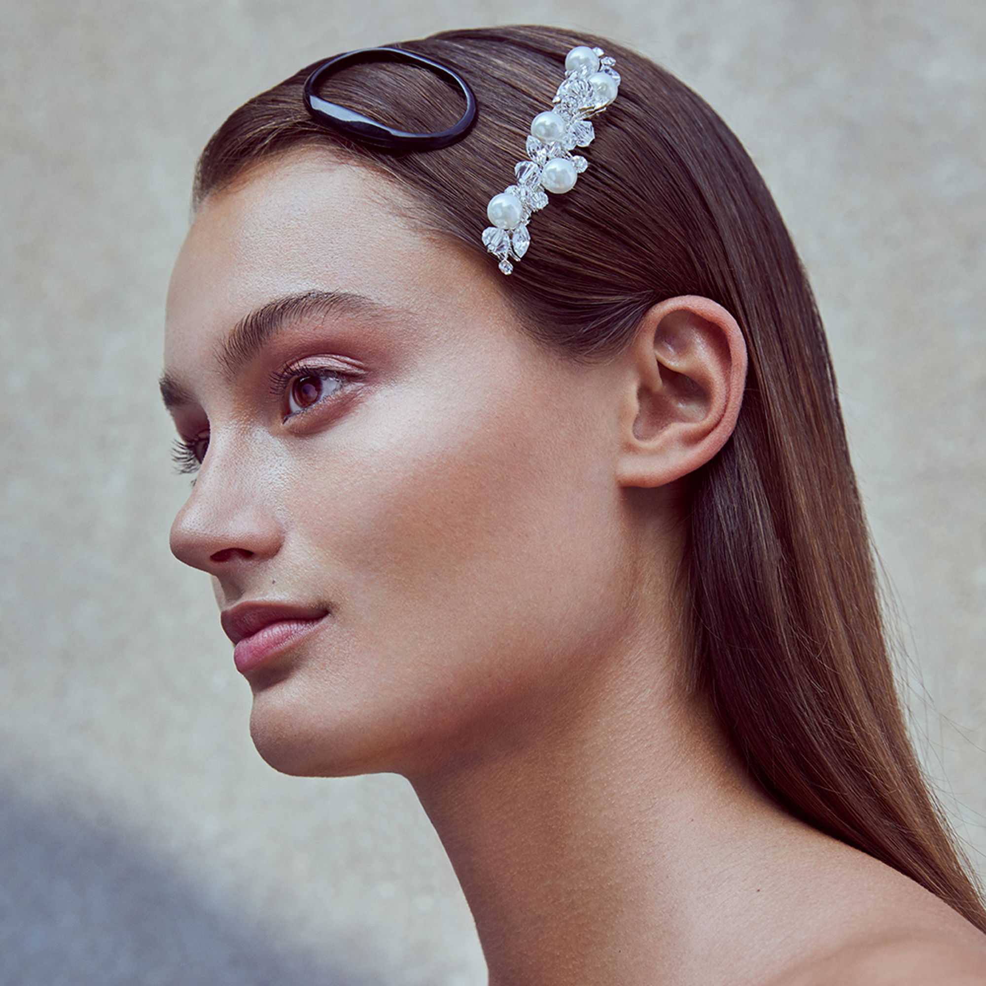 Junge Frau mit schlichtem Make-up und einer Perlen-Haarspange im glatten, braunen Haar. Der Fokus liegt auf ihrem eleganten und minimalistischen Look.