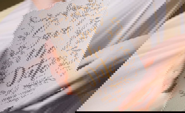 Einladungskarte im Boho-Stil mit der Aufschrift 'Save the Date', verziert mit handgezeichneten Blumenmotiven, von einer Person präsentiert.