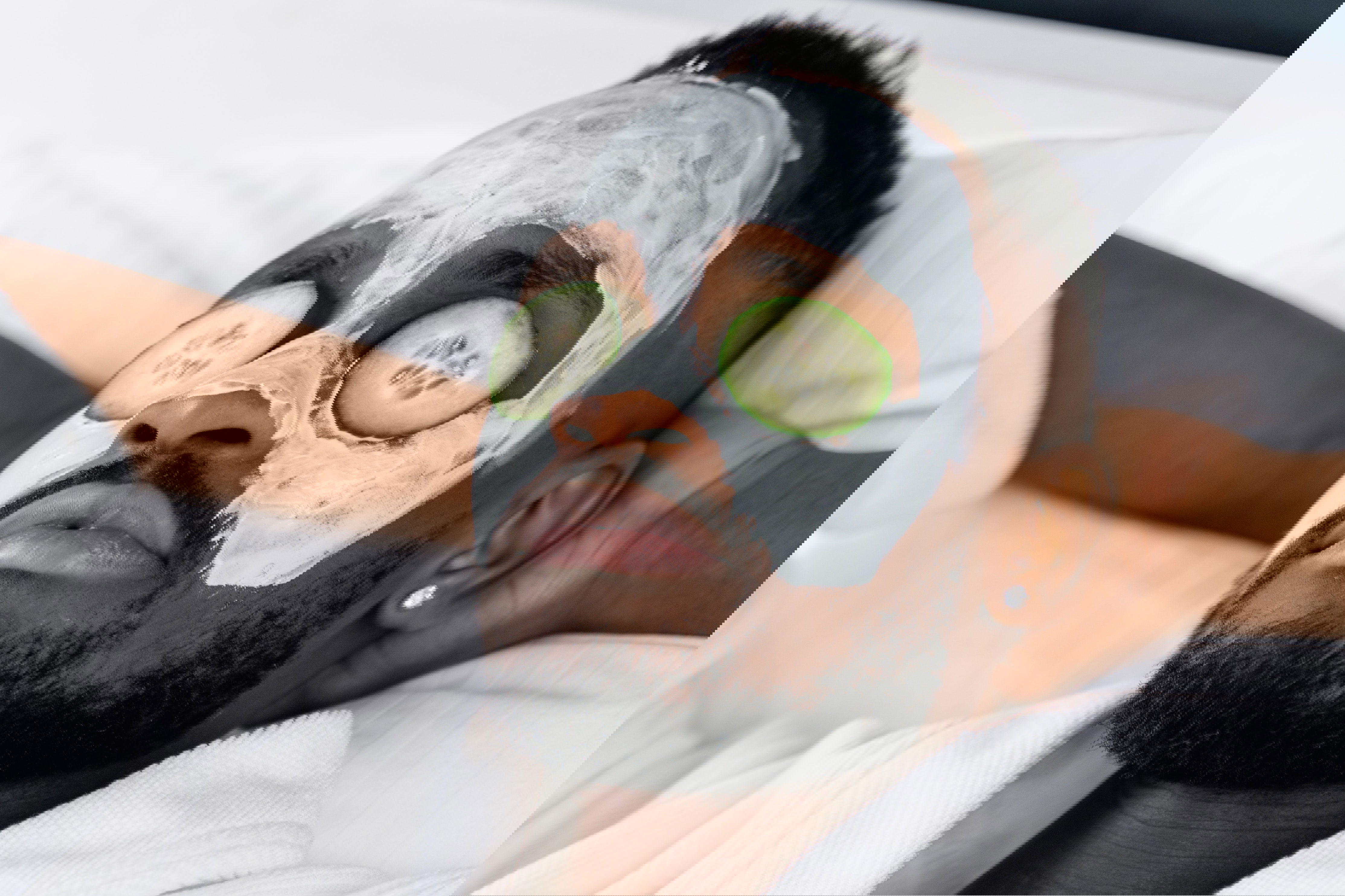 Ein Mann entspannt mit einer Gesichtsmaske und Gurkenscheiben auf den Augen, während er in einem weißen Bademantel liegt. Sein Gesichtsausdruck ist ruhig.