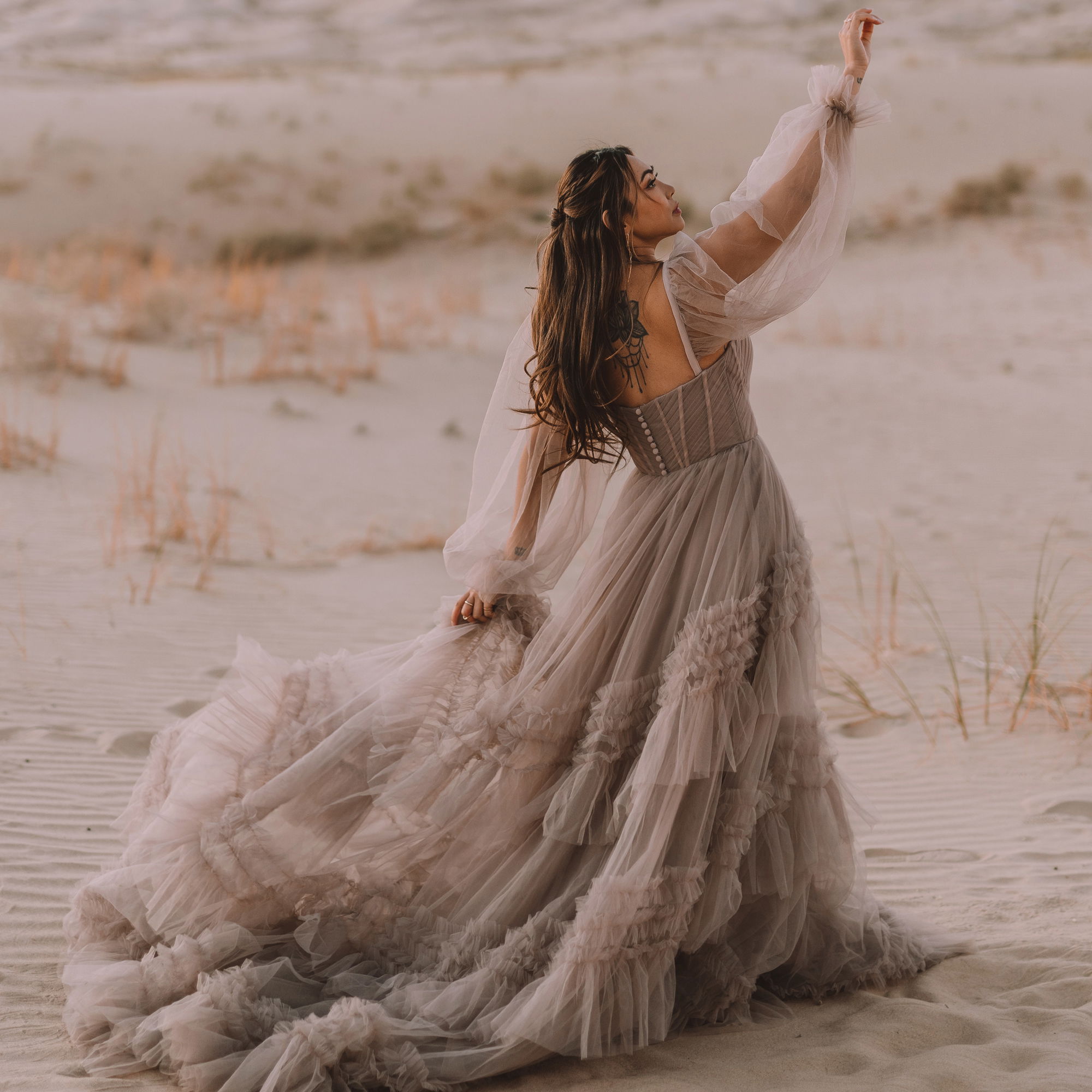 Romantisches Boho-Brautkleid mit voluminösem Tüllrock und zarten Ärmeln, getragen von einer Braut in einer sandigen Wüste.