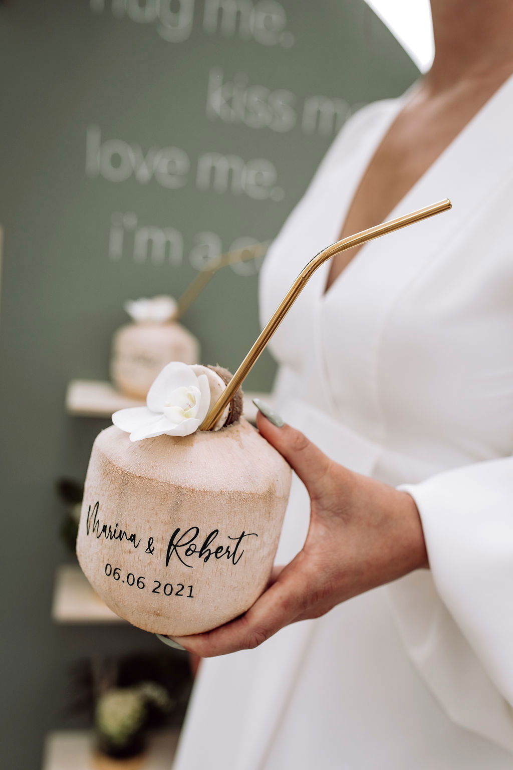 Detailaufnahme einer personalisierten Kokosnuss mit Strohhalm und weißer Blume, serviert als Drink bei einer tropischen Hochzeit.