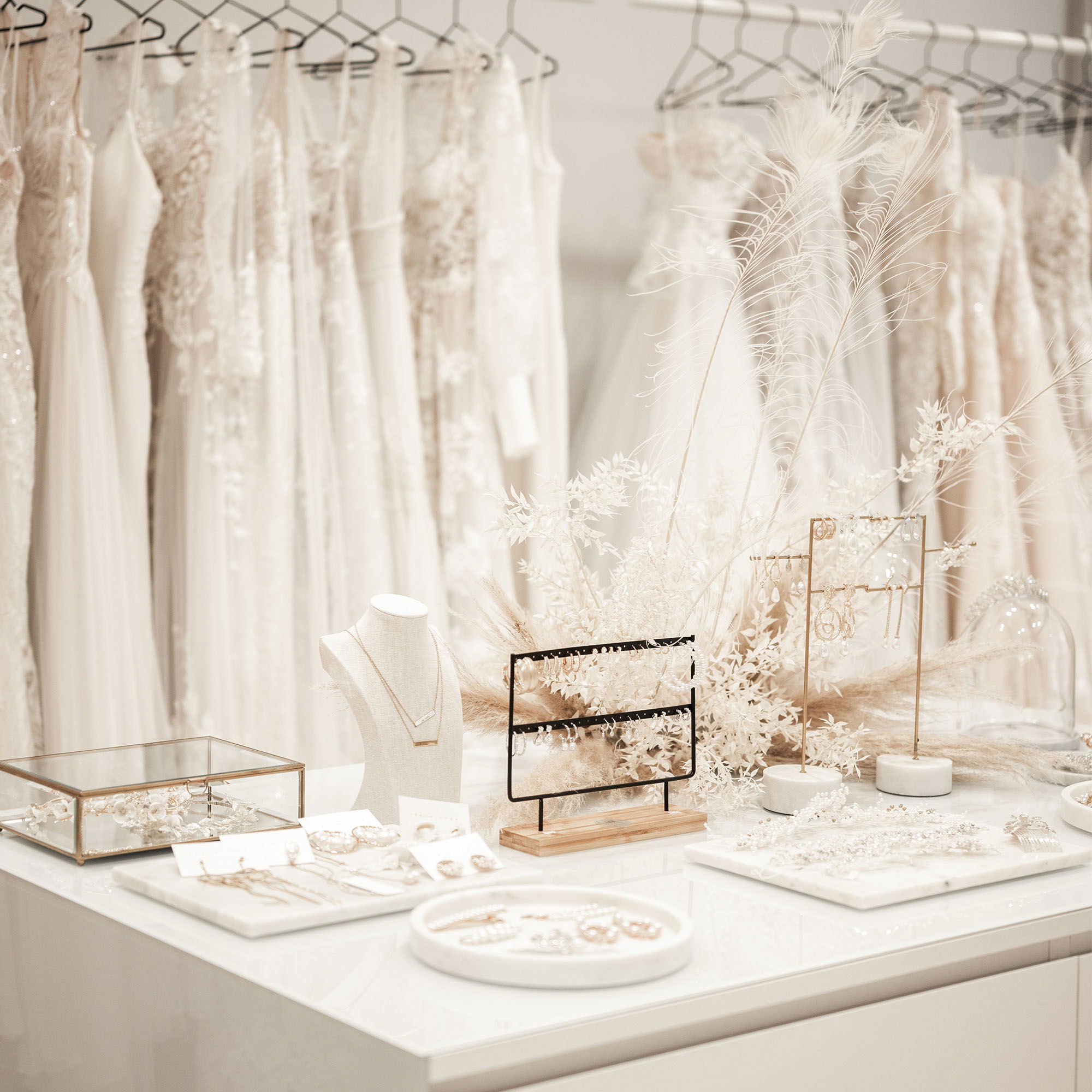 Verschiedene Brautaccessoires, einschließlich Ketten und Ohrringen, stilvoll auf einem Tisch präsentiert, umgeben von dezenter Blumen-Deko.