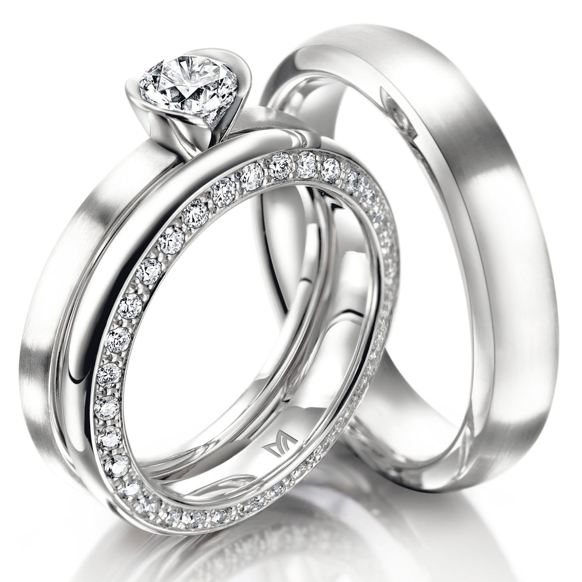 Ein Set aus Platinringen: Der Verlobungsring hat einen zentralen Diamanten, der in einer kreisförmigen Fassung sitzt, während der Ehering mit funkelnden Diamanten auf der gesamten Ringbreite besetzt ist.