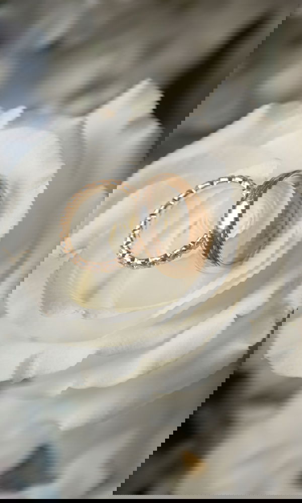 Zwei Hochzeitsringe in einer frischen, weißen Blüte arrangiert. Der eine Ring hat eine glatte, polierte Oberfläche, der andere besticht durch eine feine Struktur.