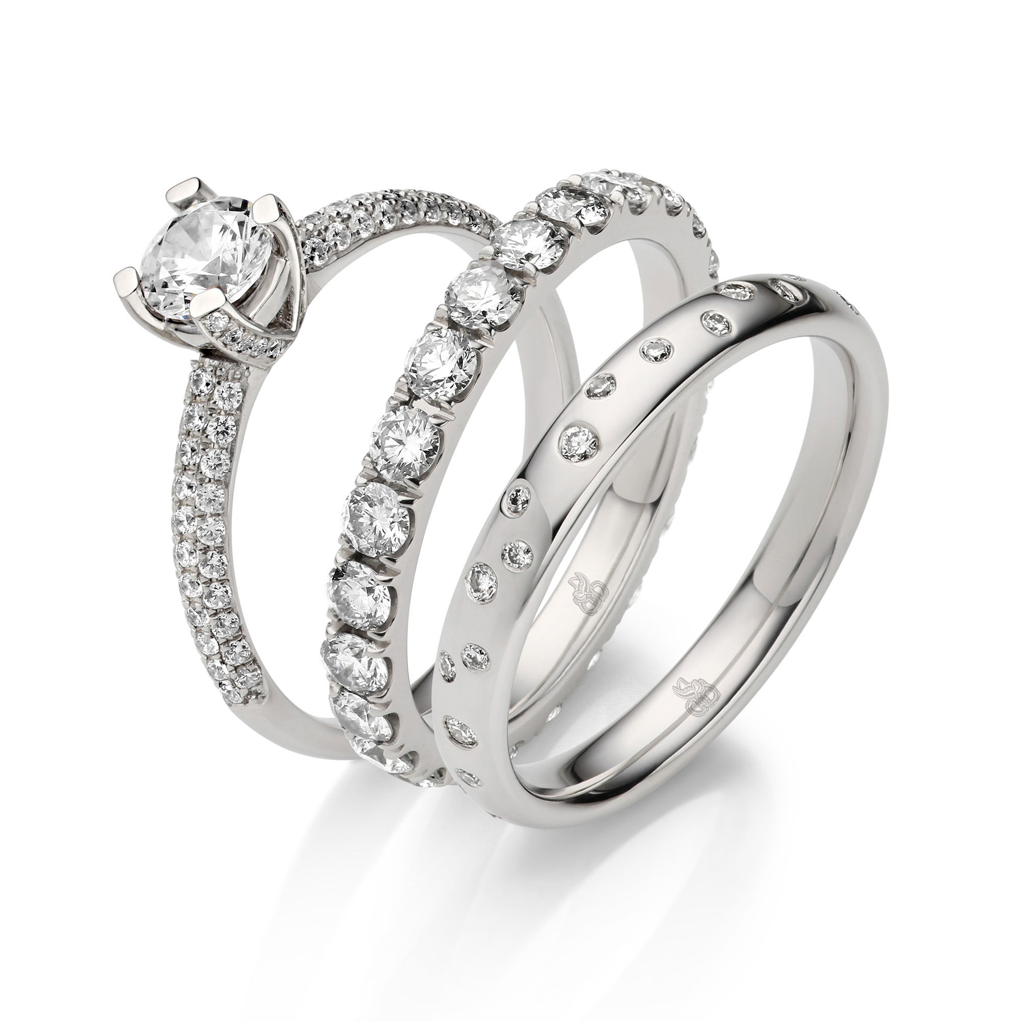 Ein Set aus drei Diamantringen: Der Verlobungsring ist mit einem großen zentralen Diamanten besetzt, und zwei Eheringe sind jeweils mit funkelnden Diamanten rundum verziert.