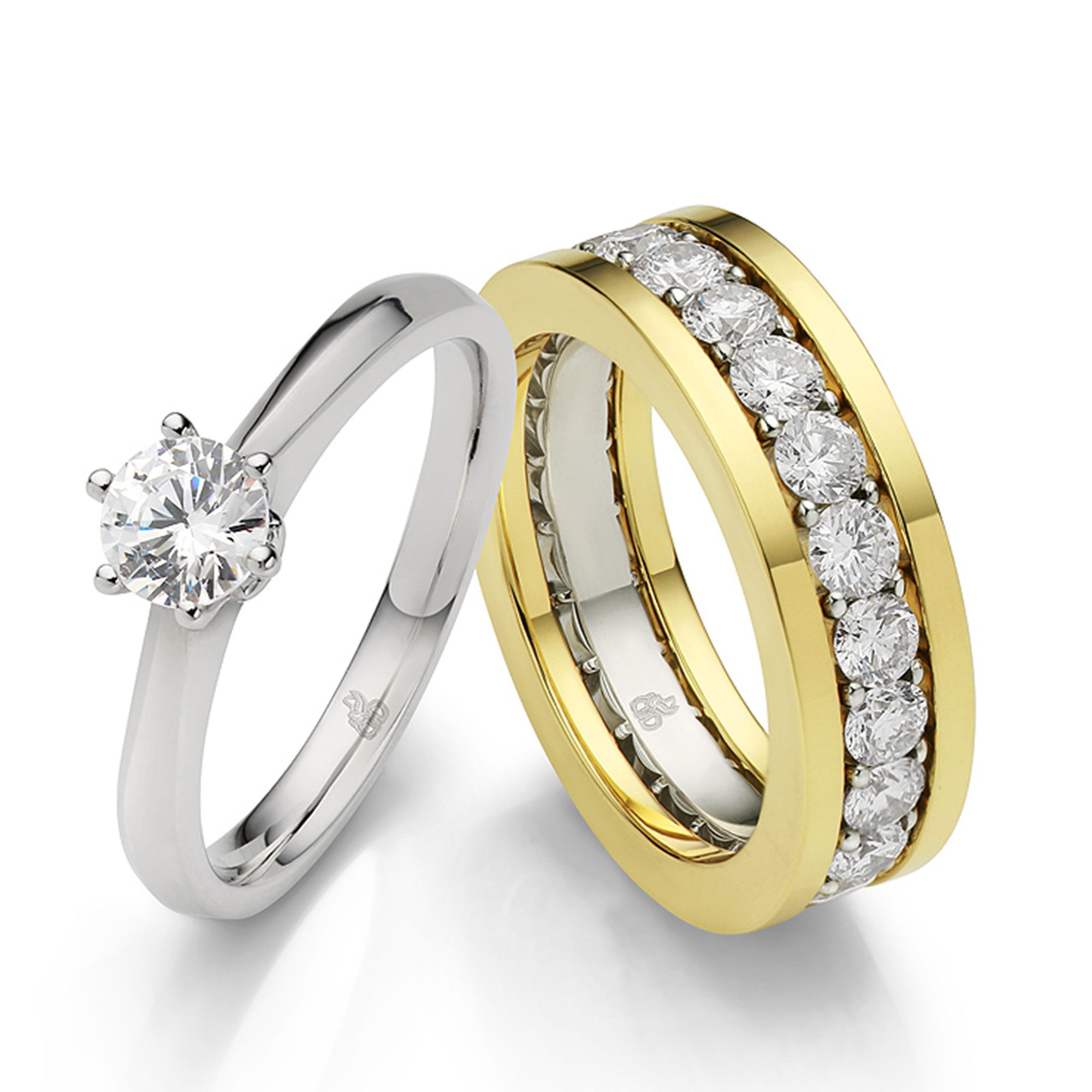 Ein schlichter Solitär-Verlobungsring aus Weißgold mit einem Diamanten wird zusammen mit einem funkelnden Gelbgold-Ehering präsentiert, der mit einer Diamantreihe besetzt ist.