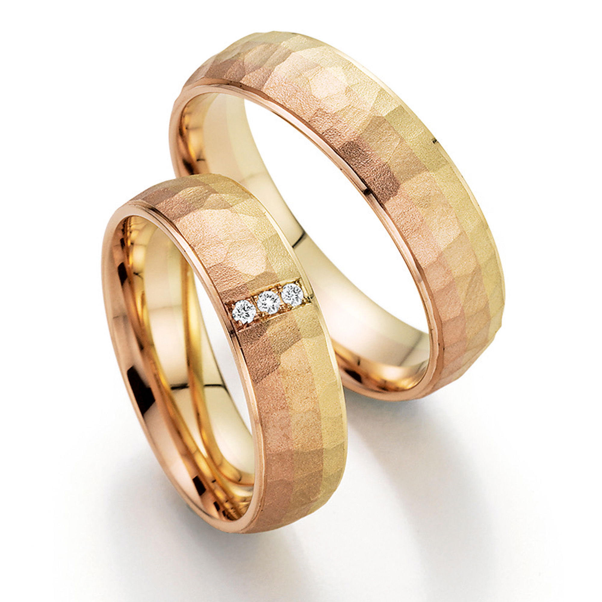 Ein Paar einzigartiger Eheringe aus Roségold mit einer gehämmerten Oberfläche. Ein Ring ist mit drei funkelnden Diamanten besetzt, die für zusätzlichen Glanz sorgen.