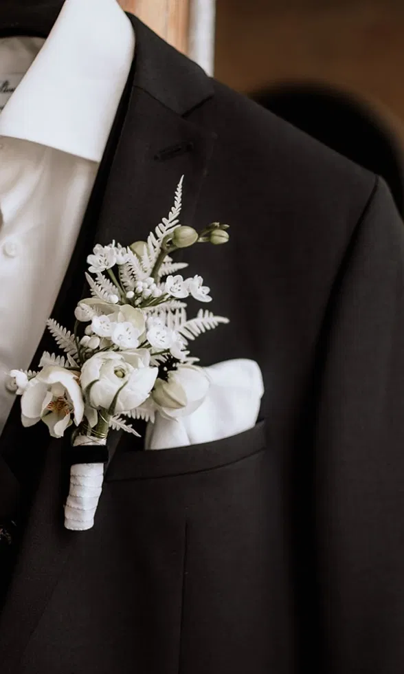 Schwarzer Smoking mit weißem Hemd, Einstecktuch und elegantem Blumenanstecker in Weiß.
