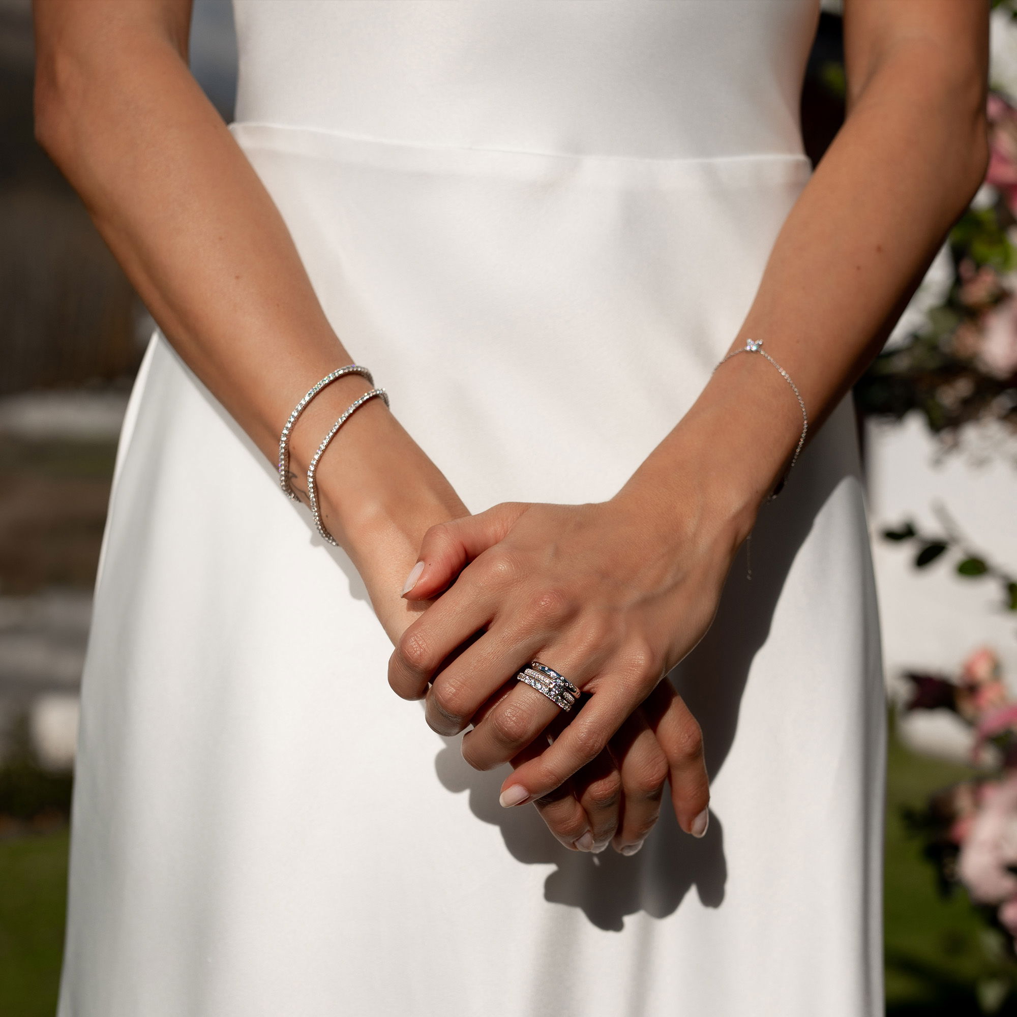 Die Braut trägt ein schlichtes, edles Hochzeitskleid. Ihre Hände ruhen ineinander, die Ringe funkeln, während ihre silbernen Armbänder den Look abrunden.