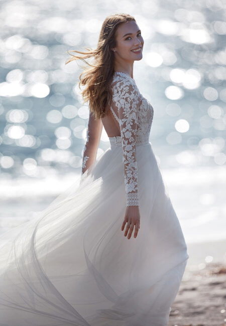 Braut im Hochzeitskleid mit Spitzenärmeln am Strand laufend