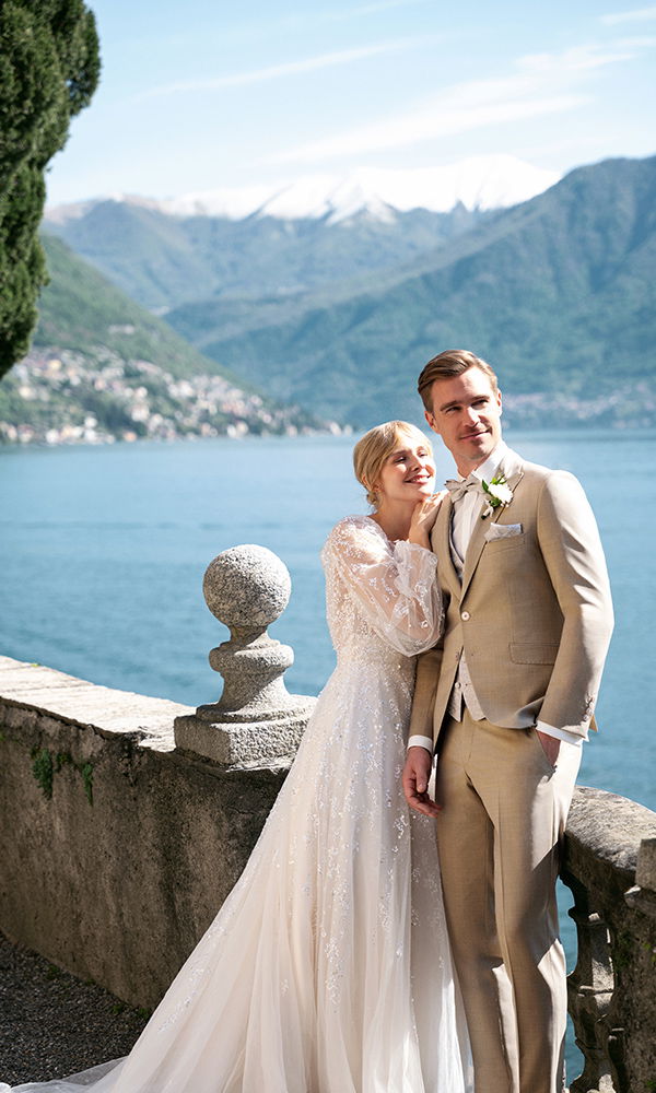 Glückliches Brautpaar am See – eleganter Hochzeitsanzug in Naturtönen.