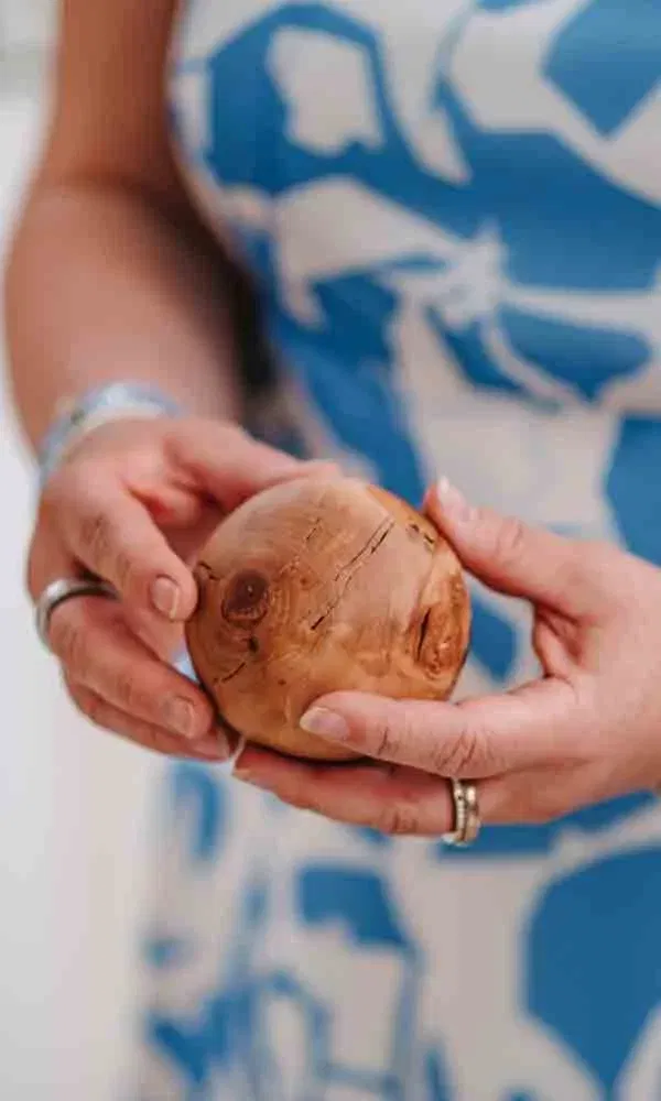 Eine Person hält eine runde Holzkugel mit Maserung behutsam in beiden Händen vor einem blauen gemusterten Kleid.
