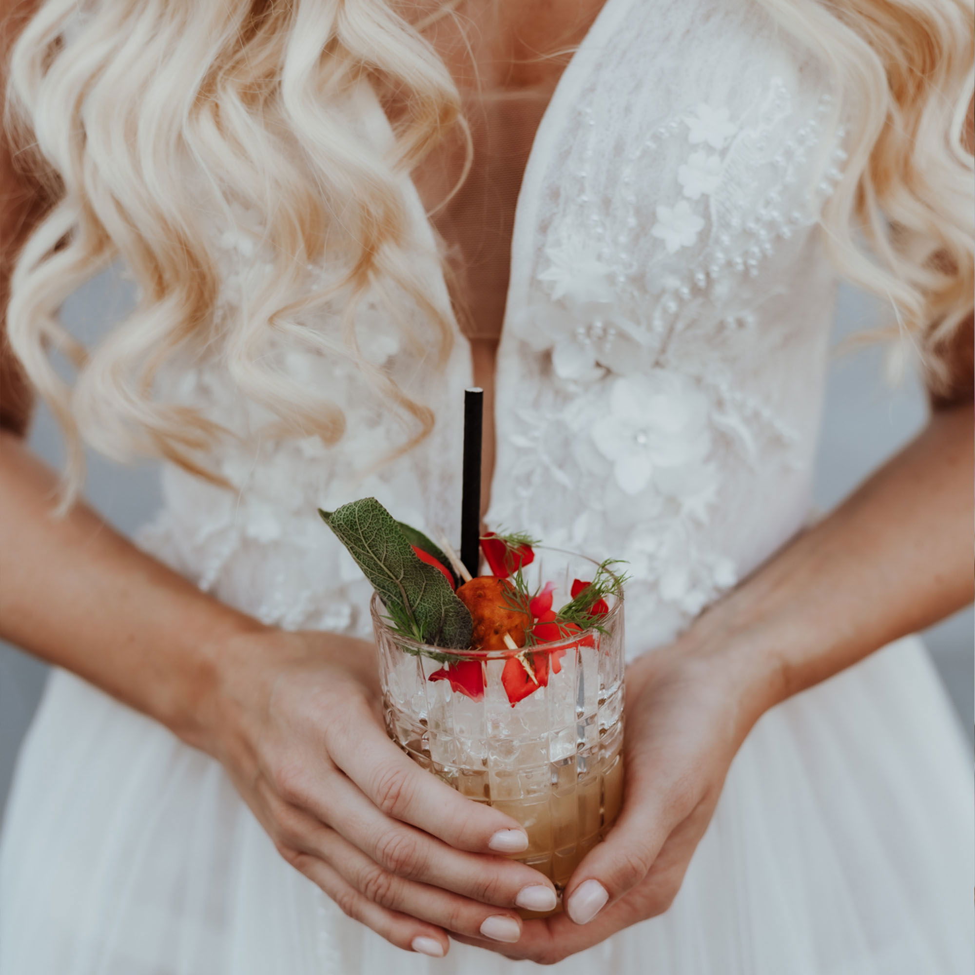 Braut in einem weißen Kleid hält einen erfrischenden Cocktail mit Minze und roten Früchten in den Händen