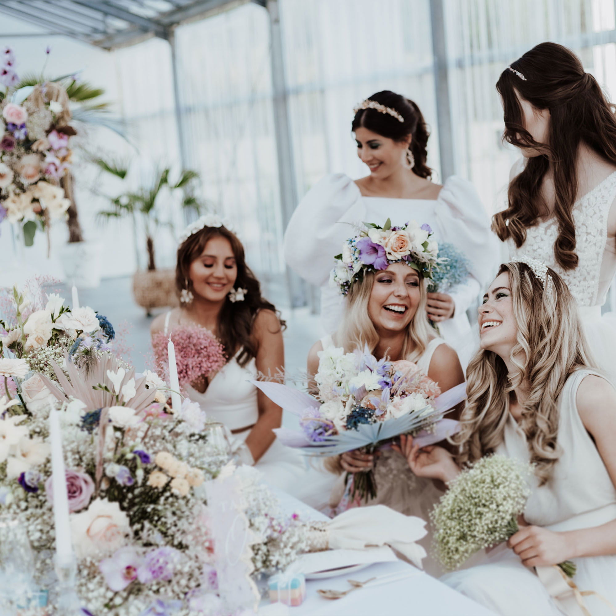 Bräute in festlichen weißen Kleidern sitzen an einem mit Blumen geschmückten Tisch und lachen fröhlich, während sie die entspannte Hochzeitsatmosphäre genießen.
