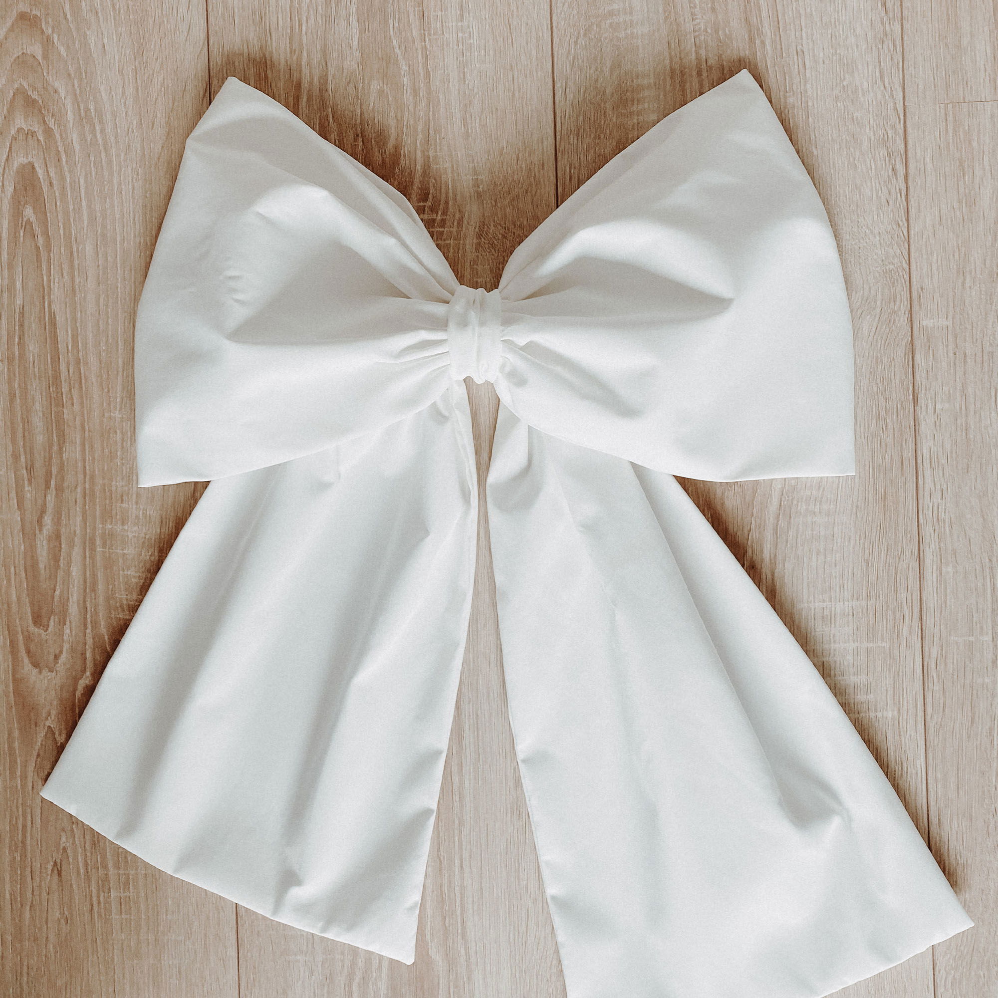 Eine elegante weiße Schleife mit breiten Bändern ist sorgfältig auf einem Holzboden ausgebreitet und wirkt schlicht und symmetrisch.