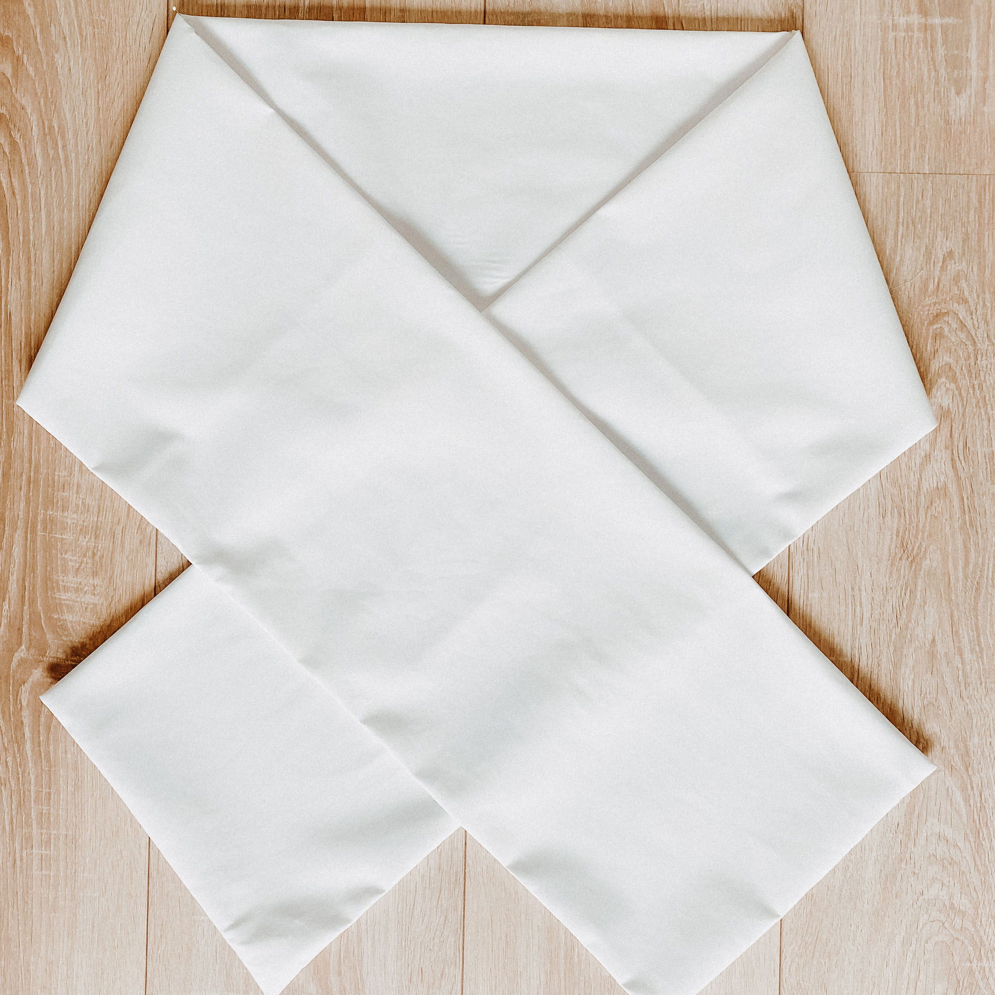 Auf einem hellen Holzboden liegt ein Stück weißer Stoff, das in einer überkreuzten Form angeordnet wurde.