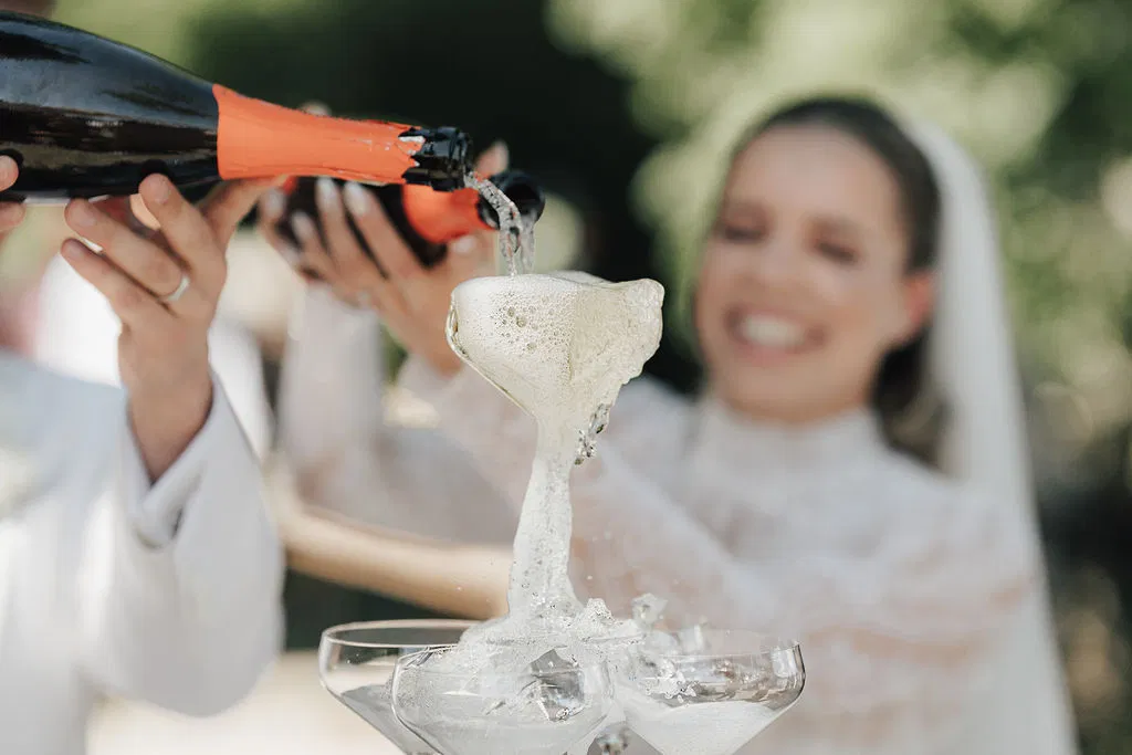 Braut und Bräutigam gießen Champagner in eine Glaspyramide, während der Schaum elegant über die Gläser fließt.