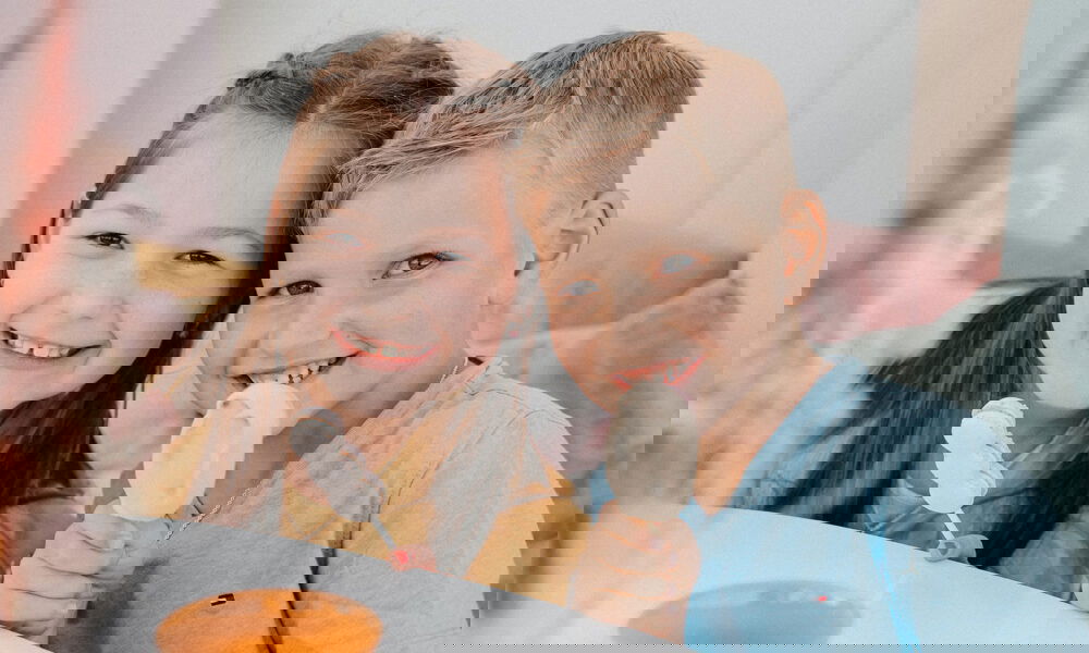 Ein Junge und ein Mädchen strahlen in die Kamera, während sie Eis am Stiel genießen, umgeben von sanften Pastelltönen.