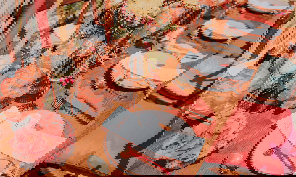 Elegante Tischdekoration für eine Hochzeit mit leuchtenden Pfingstrosen, goldenen Akzenten, handgeschriebenen Menükarten und warmen Farbakzenten auf einem Holztisch.