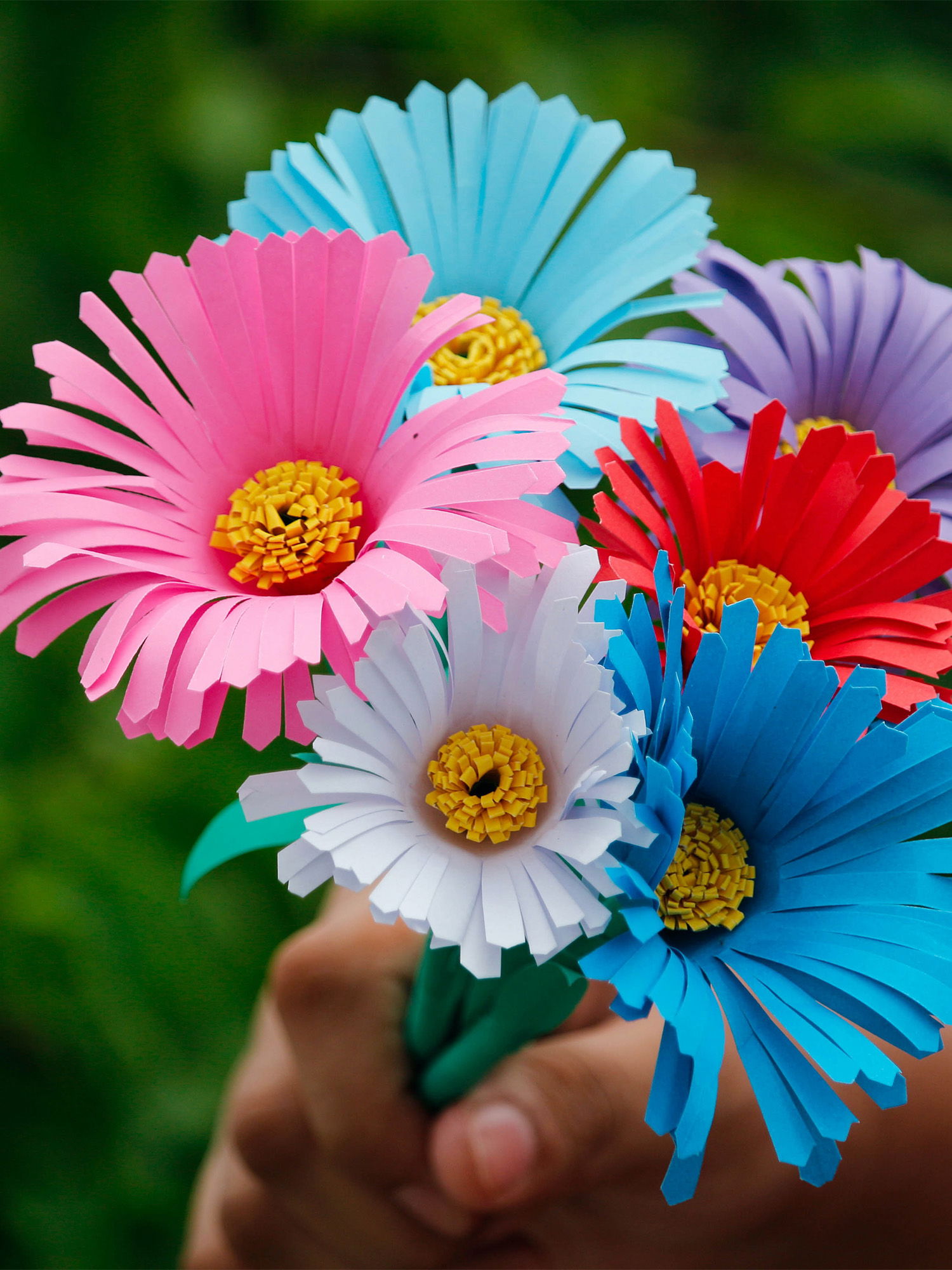 Ein kunstvoller Brautstrauß aus Papierblumen in verschiedenen Farben und Formen, der lebendige, kräftige Farbtöne wie Rosa, Blau und Gelb zeigt.