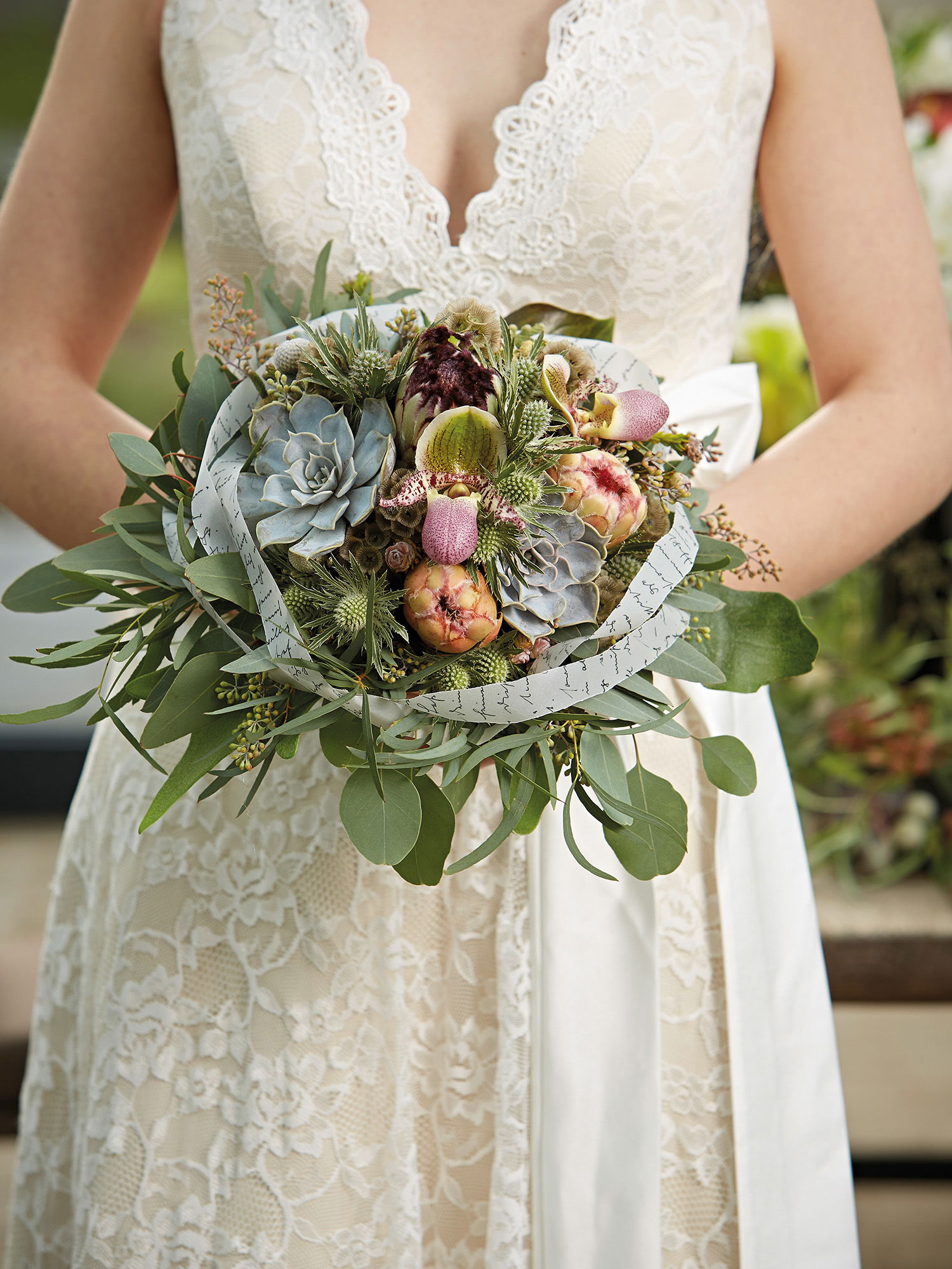 Sukkulentenstrauß mit verschiedenen Blumen, festlich arrangiert, gehalten von einer Braut in einem weißen Kleid.