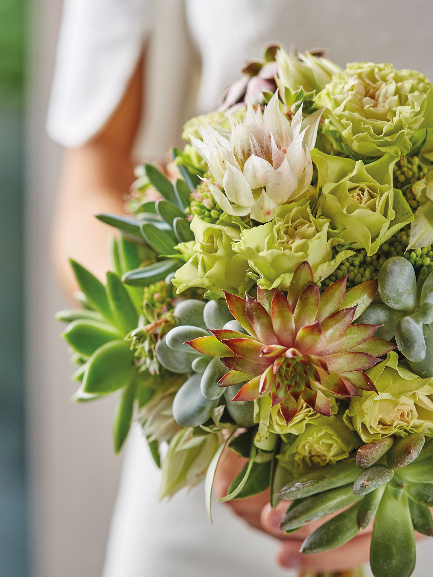 Eleganter Brautstrauß mit Sukkulenten und grünen Blüten, stilvoll arrangiert und von der Braut festgehalten.
