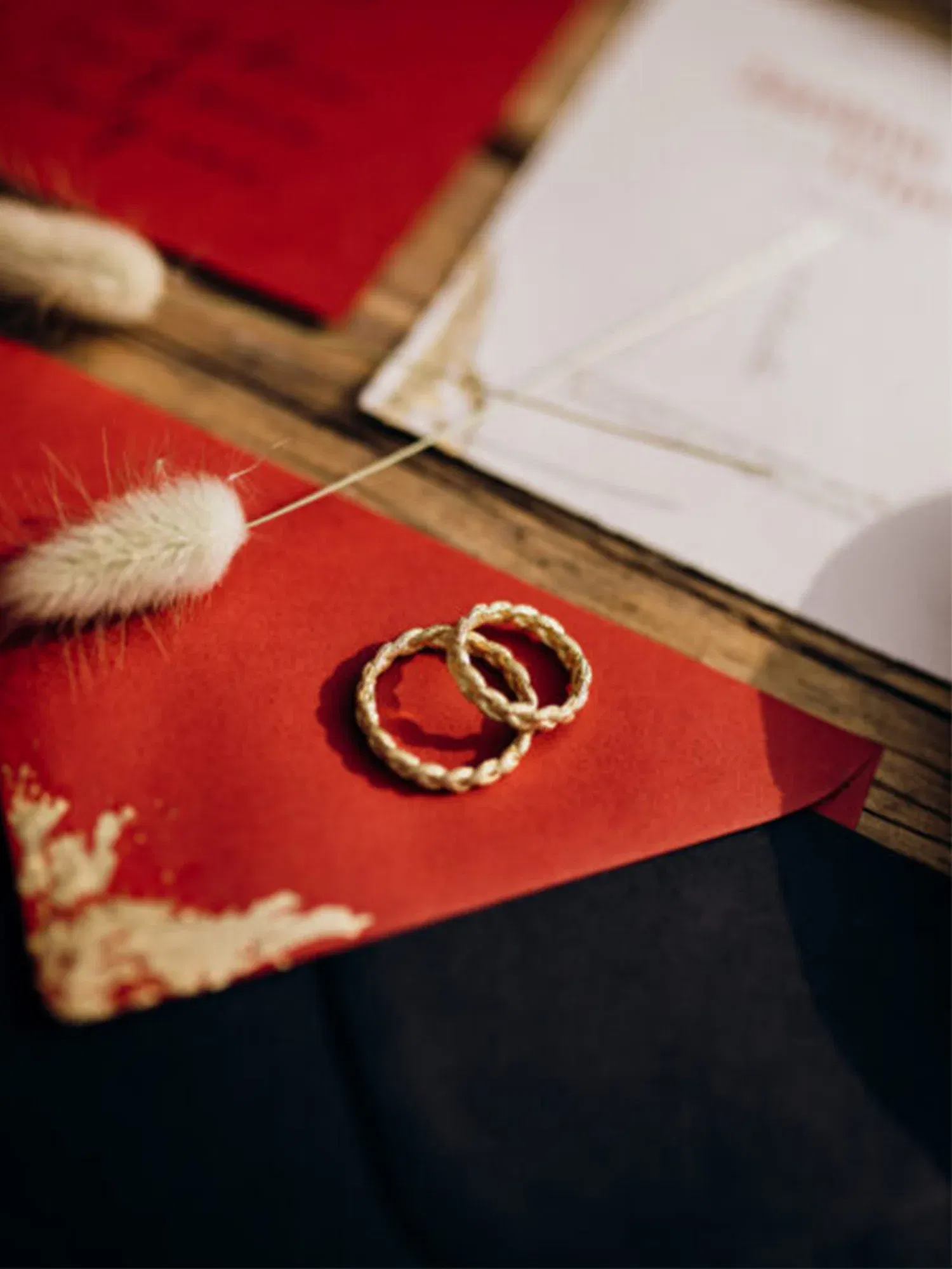 Ein Paar geflochtener goldener Ringe ruht auf einem roten Briefumschlag, der für die Hochzeitsfeier bereitliegt.
