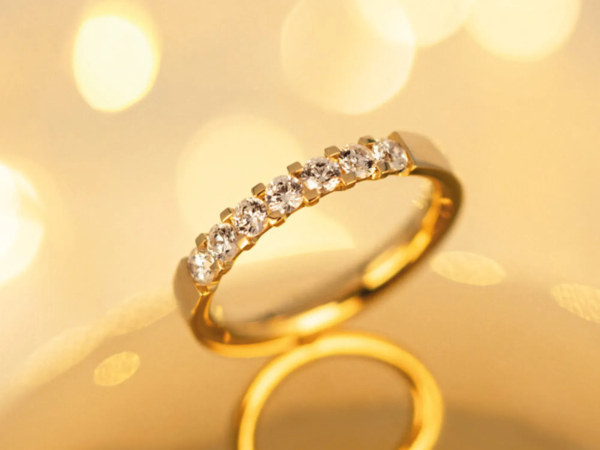Ein Goldring, verziert mit sechs strahlenden Diamanten, schwebt vor einem sanften, goldgelben Hintergrund mit Lichteffekten, die den Glanz der Edelsteine hervorheben.