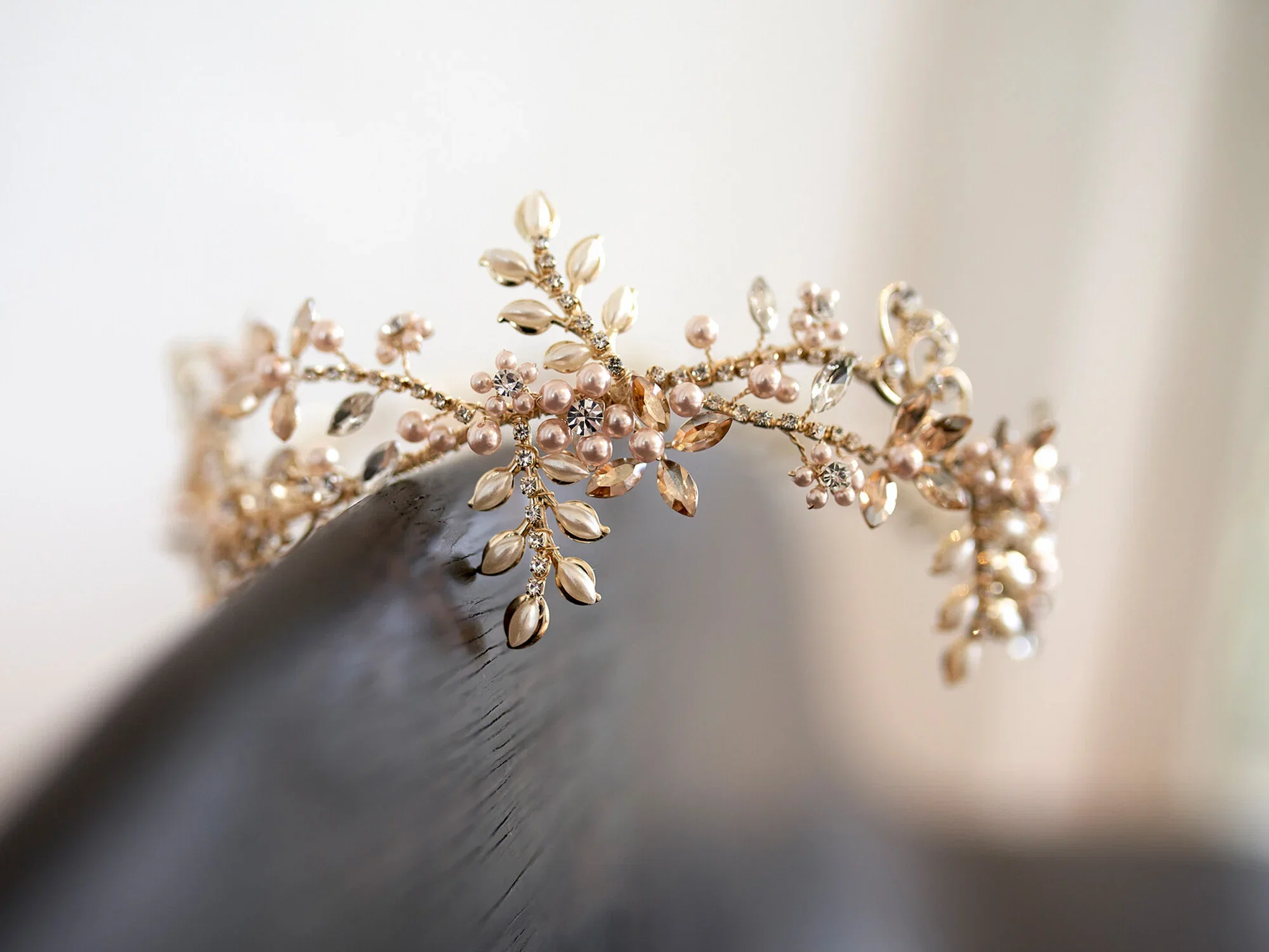 Eine goldene Tiara, verziert mit Perlen und kleinen Kristallen in Blumenform, die auf einem dunklen Untergrund liegt. Perfekt für eine Braut.