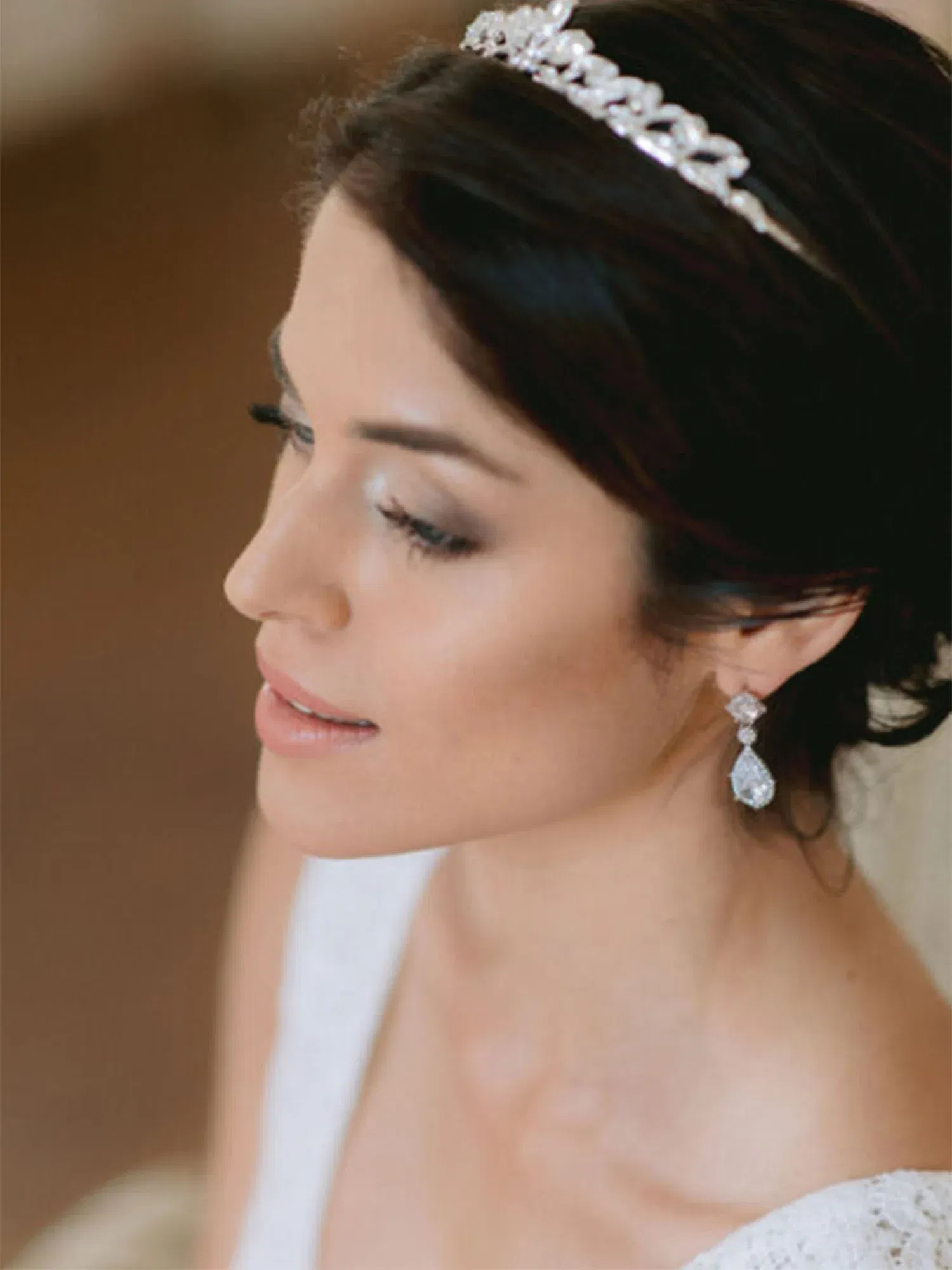 Nahaufnahme einer Braut mit einer eleganten Tiara und Diamantohrringen, die ihre Hochsteckfrisur betont. Sie trägt ein weißes Hochzeitskleid.