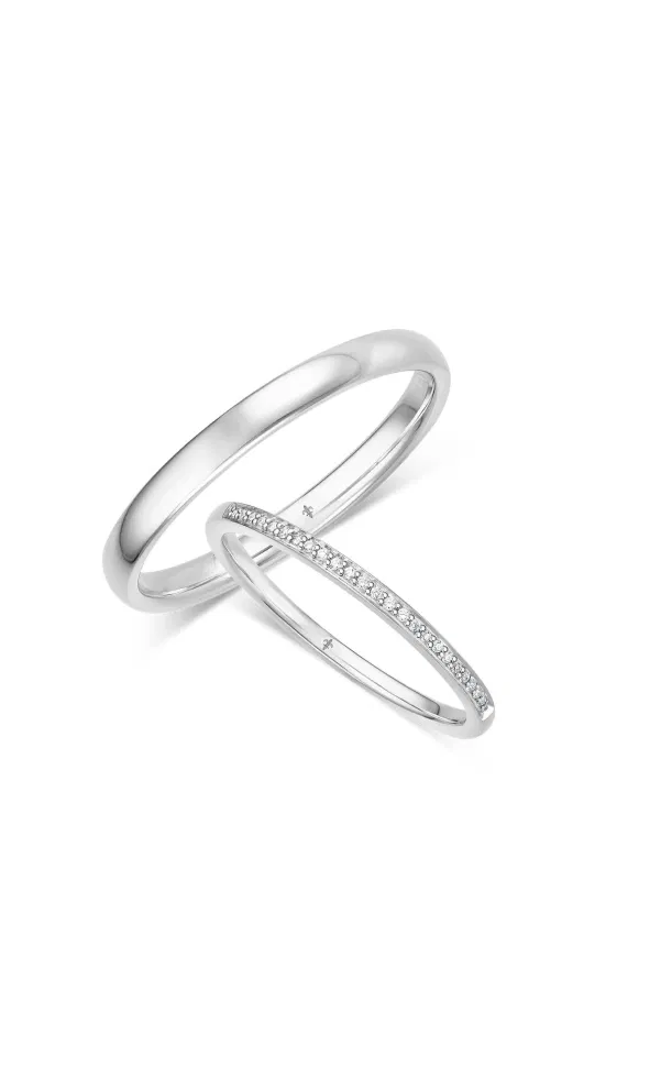 Zwei moderne Eheringe aus Weißgold, einer glatt und poliert, der andere mit einer feinen Reihe eingefasster Diamanten, elegant vor hellem Hintergrund dargestellt.