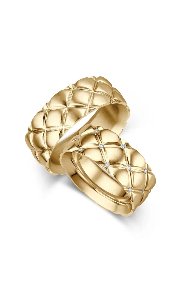 Zwei markante Eheringe aus Gelbgold mit plastischer, quiltartiger Struktur, einer davon mit mehreren eingefassten Diamanten, ausdrucksstark im Statement-Design vor hellem Hintergrund.