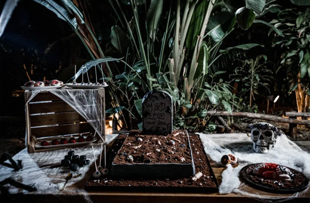 Gothic-inspirierter Sweet Table mit einem Grabstein, Totenkopf und Spinnweben. Dunkle, mystische Atmosphäre mit grünen Pflanzen im Hintergrund.