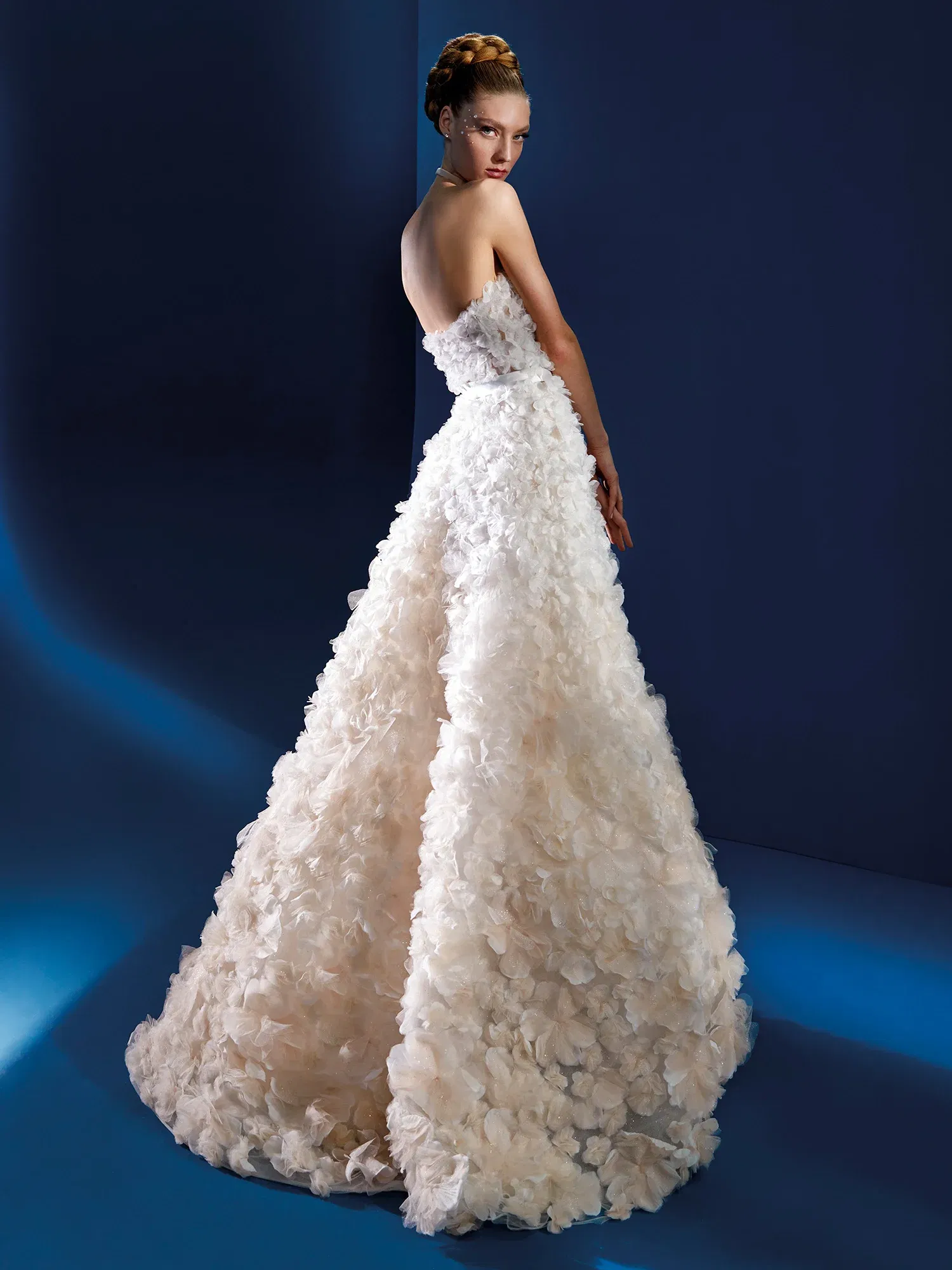 Elegantes, trägerloses Brautkleid mit einem detailreichen, blütenverzierten Rock. Die voluminösen Blütenapplikationen schaffen einen dramatischen Effekt und unterstreichen die romantische Silhouette des Kleides.