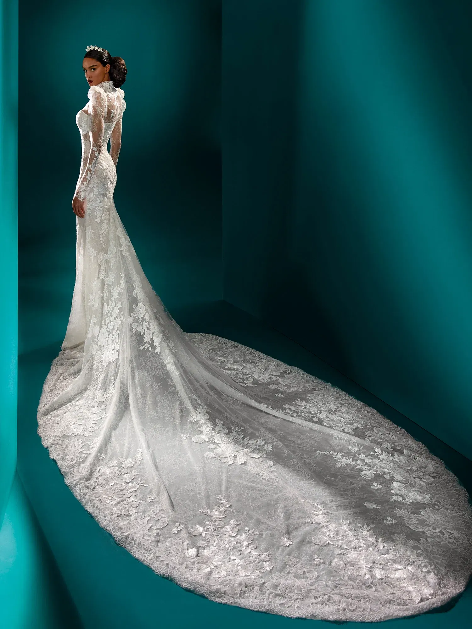 Luxuriöses Brautkleid mit aufwendig gearbeiteter, bodenlanger Spitzenschleppe. Das figurbetonte Design betont die Taille, während die langen Spitzenärmel und der transparente Rücken dem Kleid eine elegante und zeitlose Ausstrahlung geben.