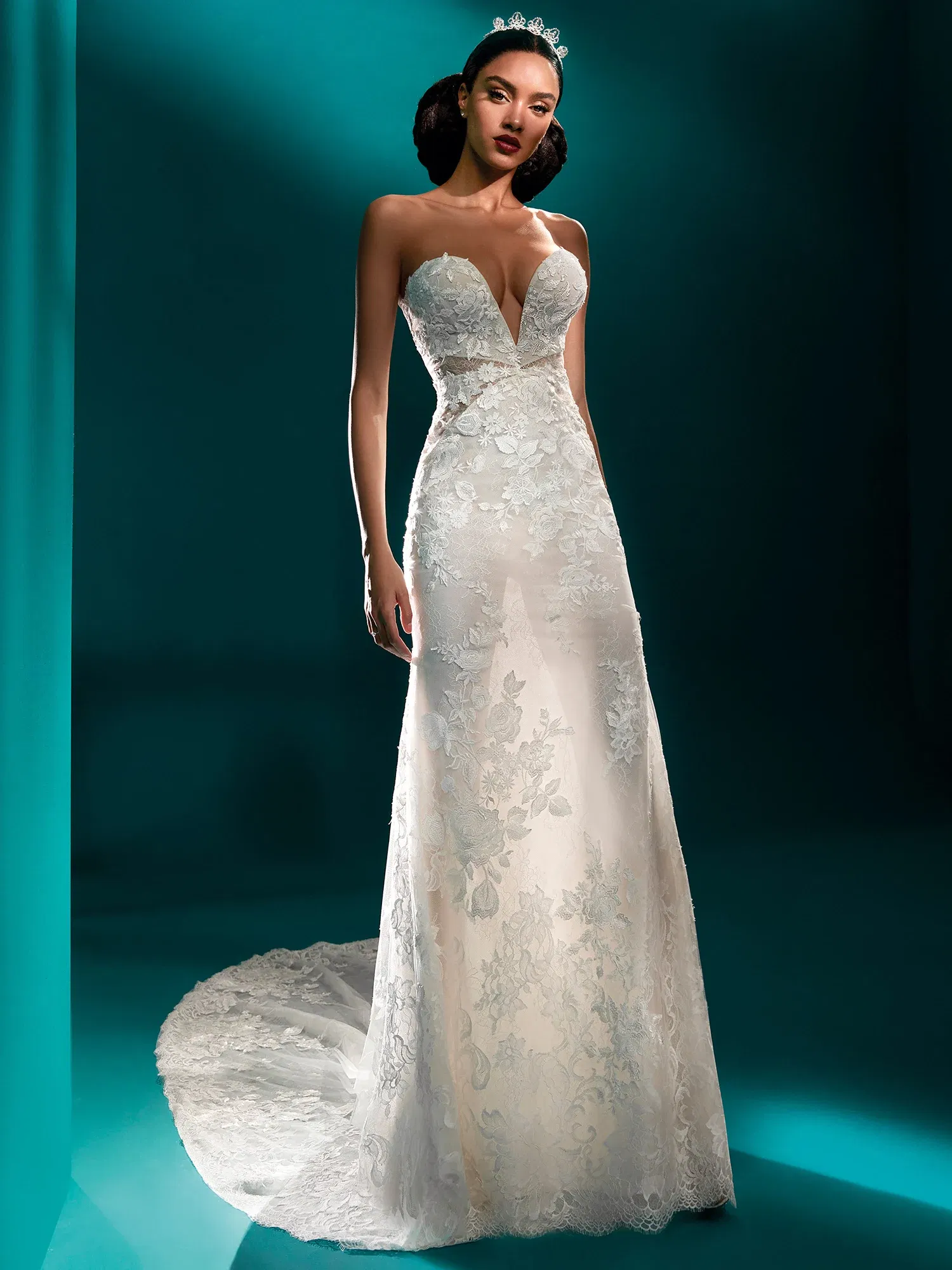 Elegantes Brautkleid mit tiefem Ausschnitt und floralen Spitzenmustern, das die weibliche Silhouette betont. Die zarte Spitze zieht sich über den gesamten Körper und endet in einer langen Schleppe, die den Boden sanft berührt.