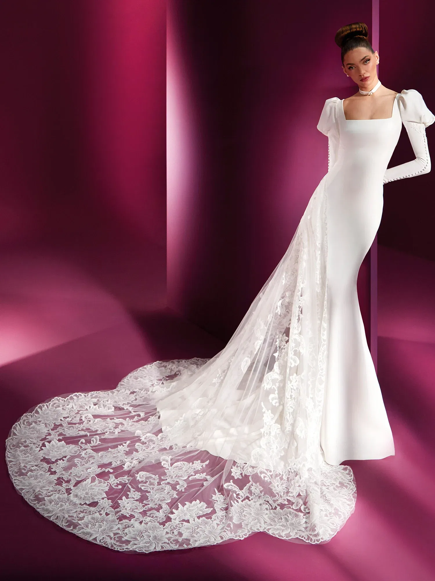 Elegantes, figurbetontes Brautkleid mit langen Ärmeln und einem quadratischen Ausschnitt. Die Braut trägt einen langen, floralen Spitzenschleier, der dem modernen Design einen klassischen Touch verleiht.