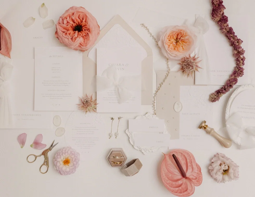 Romantisches Arrangement aus Hochzeitskarten, Umschlägen und floralen Elementen in Apricot- und Rosétönen, kombiniert mit Schere, Siegel und Schmuckdetails.